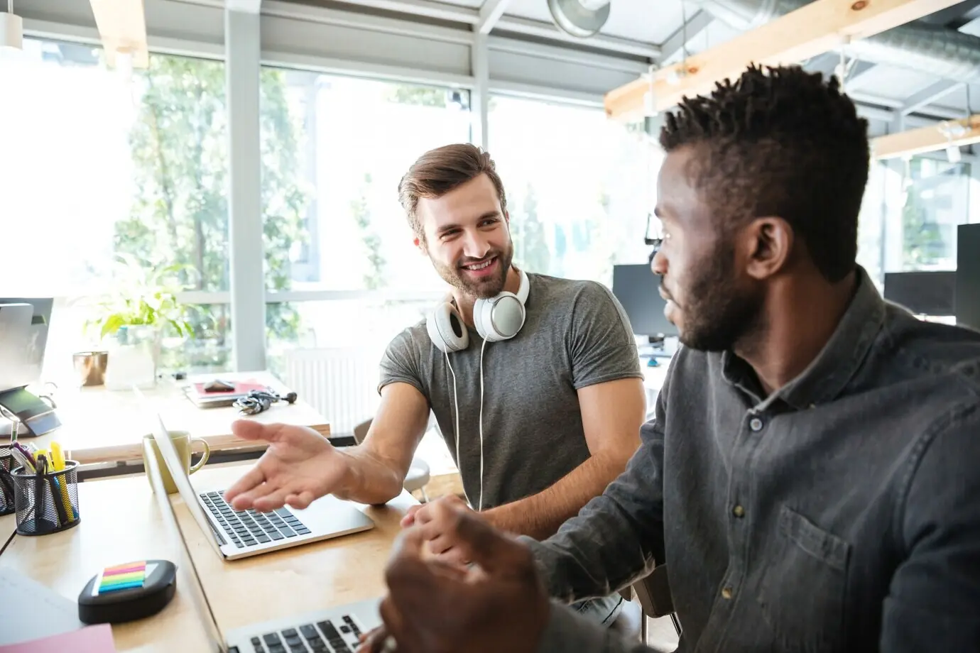 Fröhliche junge Kollegen sitzen im Coworking-Büro und benutzen einen Laptop.